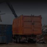 Dynamic Metal Recycling | A large orange dumpster and a smaller blue dumpster are surrounded by piles of scrap metal. A crane arm lifts debris into the orange dumpster, showcasing efficient metal recycling in progress.